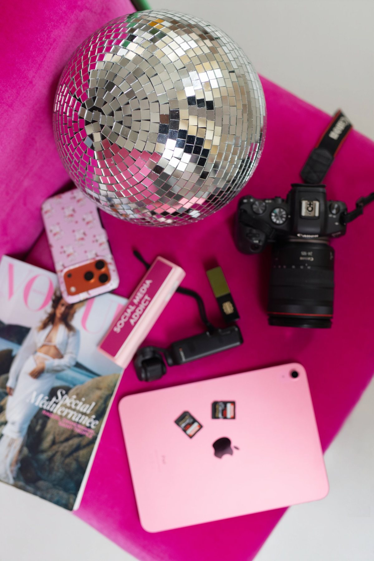 Boule à facettes, appareil photo, tablette rose et magazine sur un fauteuil rose
